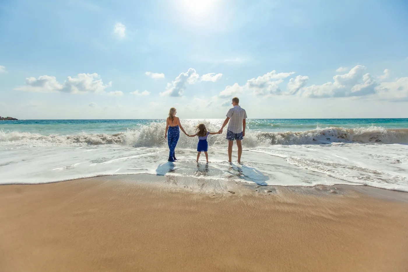 A family walking hand in hand into the waves at a sunny beach