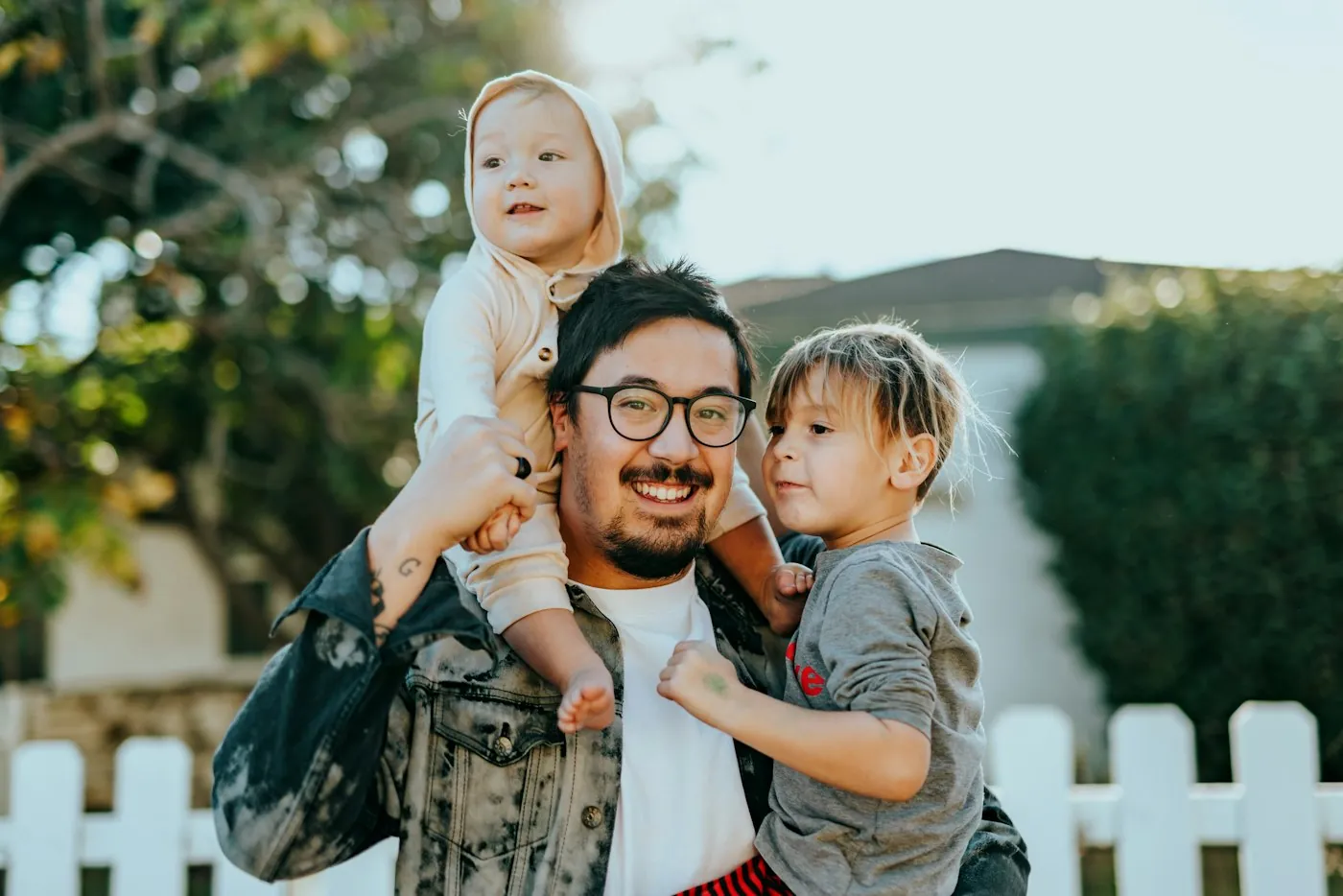 A smiling dad with his two young children outdoors on a sunny afternoon